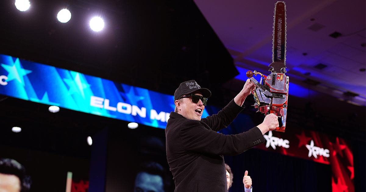 Elon Musk brandishes a chainsaw on stage. Credit / Getty Images