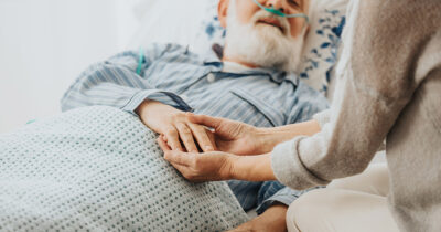 Nurse holds old man's hand. (Stock Image). Credit / Shutterstock