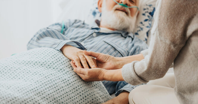 Nurse holds old man's hand. (Stock Image). Credit / Shutterstock