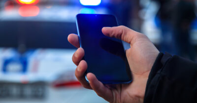 Man holds phone while sirens blare. (Stock Image). Credit / Shutterstock