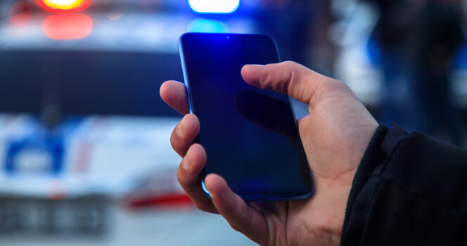 Man holds phone while sirens blare. (Stock Image). Credit / Shutterstock