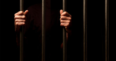 Hands grip prison bars. (Stock Image) Credit / Shutterstock