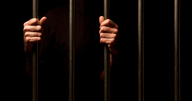 Hands grip prison bars. (Stock Image) Credit / Shutterstock