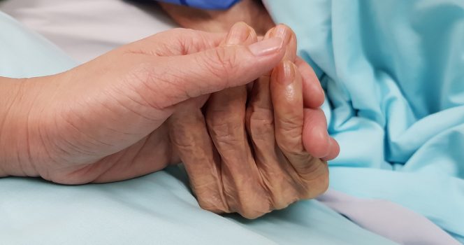 A nurse holds a patient hand. Credit / Shutterstock