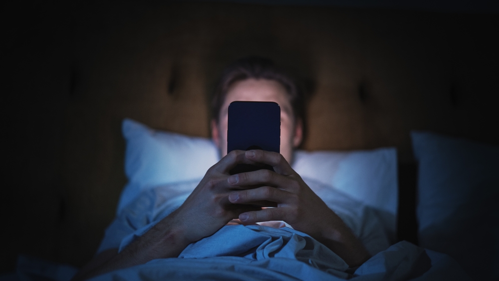 mężczyzna przegląda telefon lężąć w łóżku