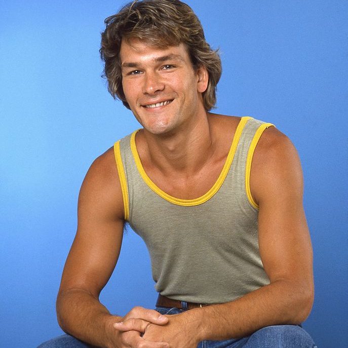 uśmiechnięty Patrick Swayze w szarej koszulce na ramkach i żółtej lamówce na niebieskim tle