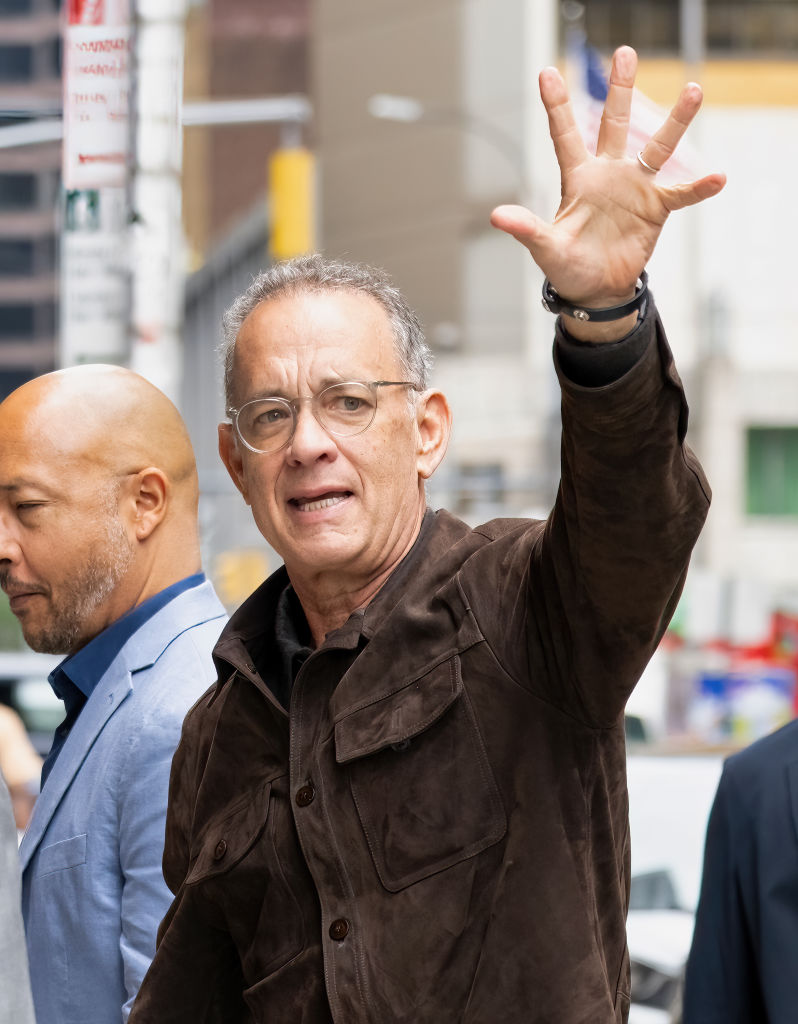 Tom Hanks w okularach z uniesioną ręką do góry
