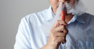 mężczyzna w białej koszuli używa waporyzatora