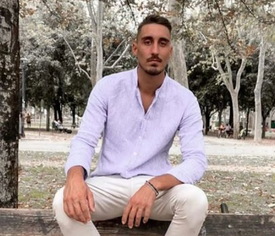 Andrea Mazzetto siedzi na drewnianej ławce na tle drzew
