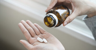 Lääkepurkki ja pillerit naisen kädessä. Shutterstock