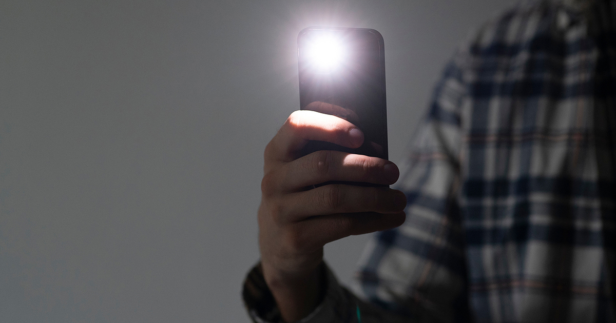 Hånd holder mobiltelefon med tændt lygte