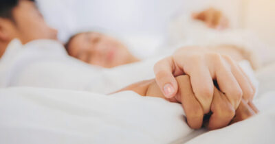 Coppia che si tiene per mano a letto.